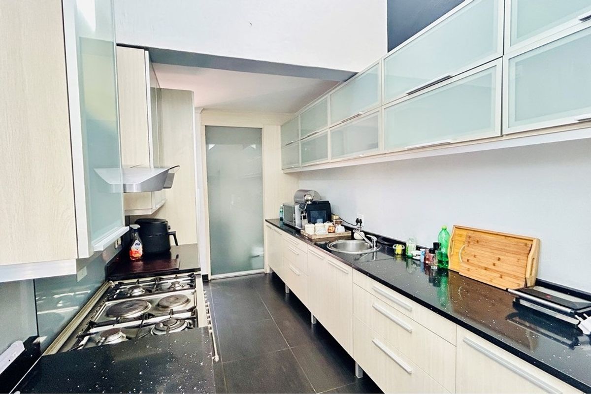 A modern galley-style kitchen featuring sleek cabinetry, dark stone countertops, a built-in gas hob, and an integrated extractor fan.