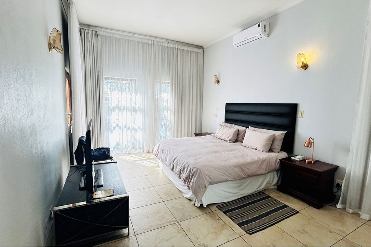 A well-lit bedroom featuring tiled flooring, wall-mounted air conditioning unit, and large floor-to-ceiling curtains leading to an outdoor area.