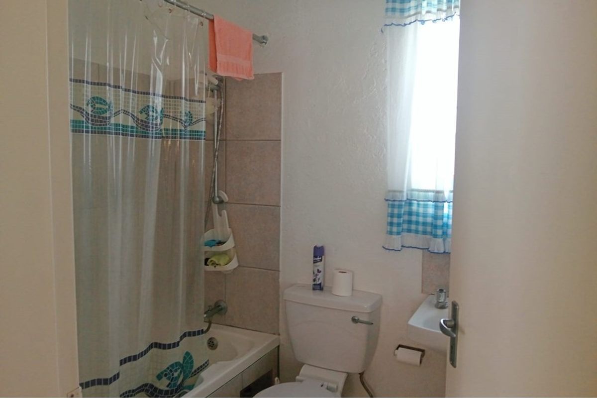 A compact bathroom featuring a shower-over-tub combination, a standard toilet, and a small wall-mounted basin with tiled splashback.