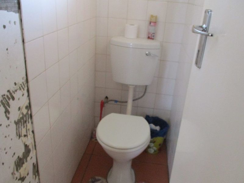 A small bathroom featuring a standard toilet, tiled walls, and tiled flooring, currently requiring wall repairs and cosmetic updates.