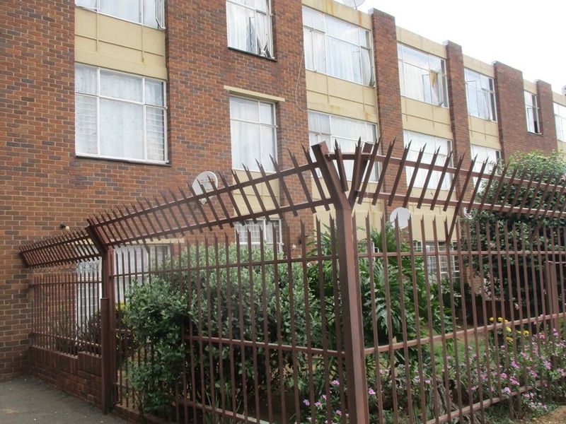 Exterior view of a multi-story apartment building featuring a face brick facade and secure perimeter fencing with spiked security topping.