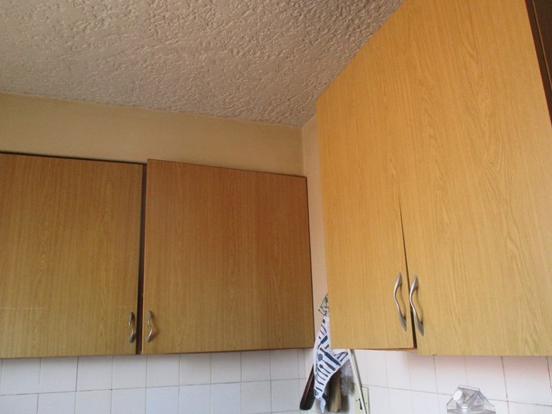 A close-up view of dated kitchen cabinetry with a tiled backsplash and textured ceiling, showing signs of wear and age.