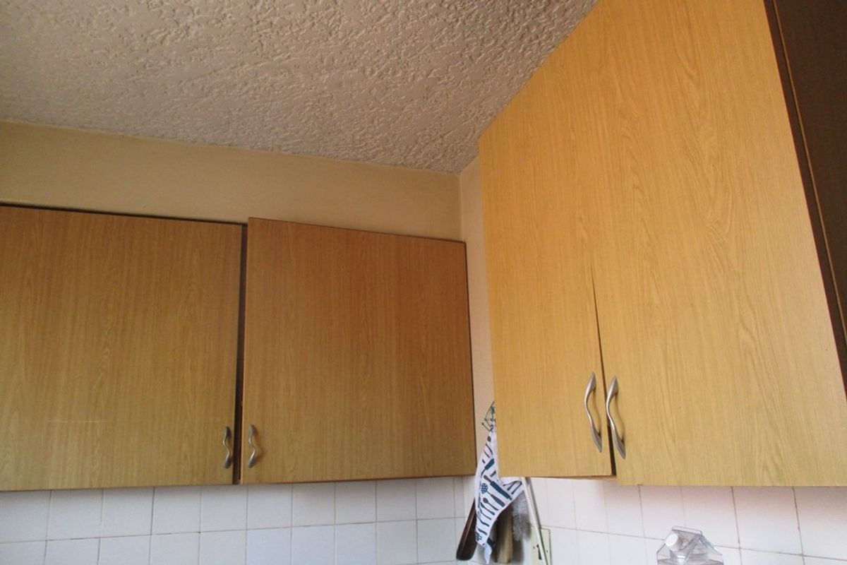 A close-up view of dated kitchen cabinetry with a tiled backsplash and textured ceiling, showing signs of wear and age.