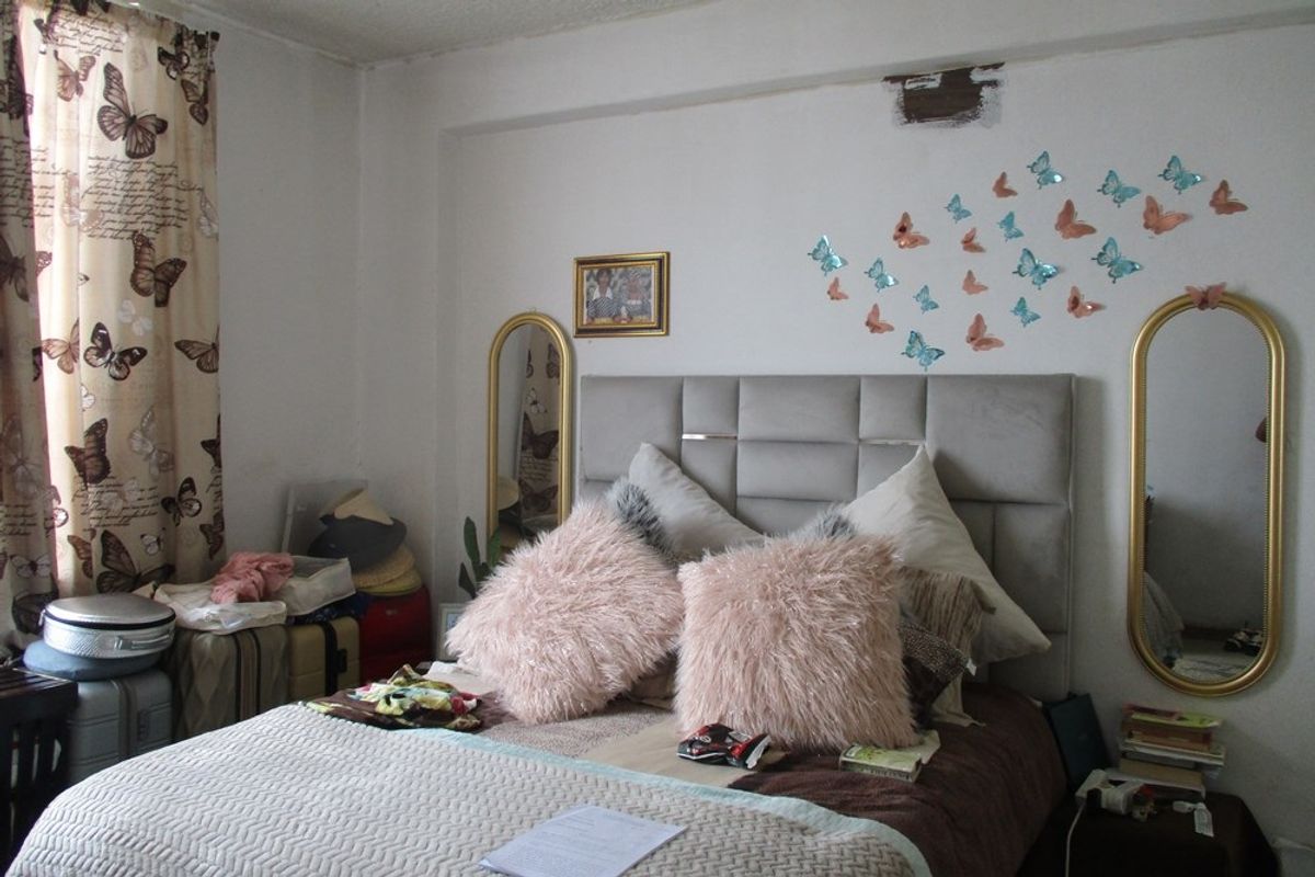A bedroom featuring a neutral wall finish with visible plaster damage above the bed area.