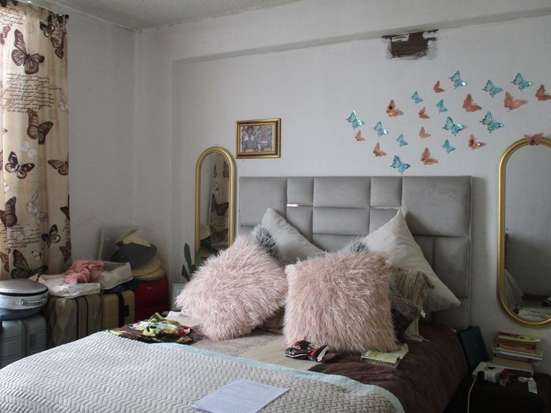 A bedroom featuring a neutral wall finish with visible plaster damage above the bed area.