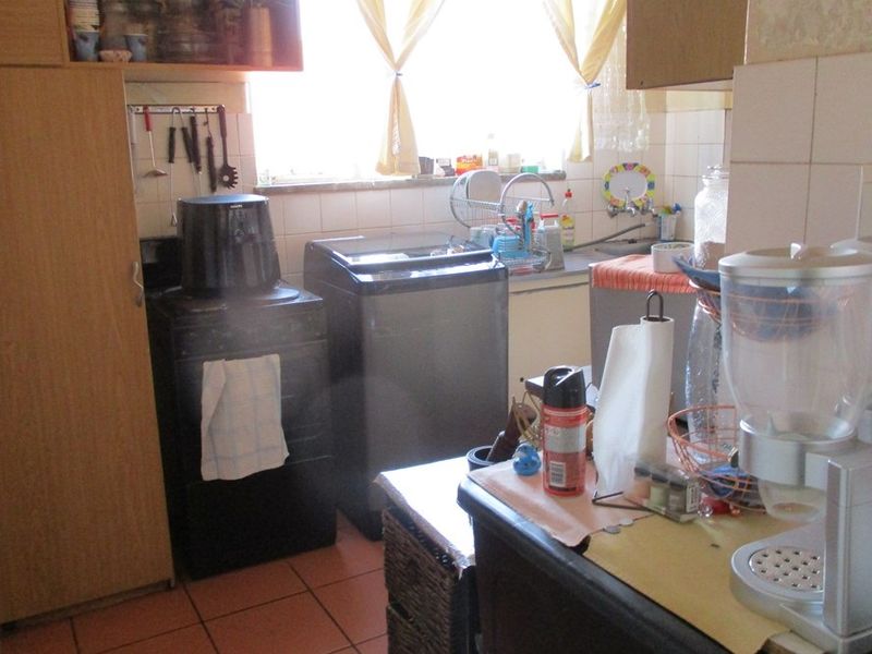 A dated kitchen featuring tiled flooring, a tiled backsplash, and built-in cabinetry with a functional sink area.