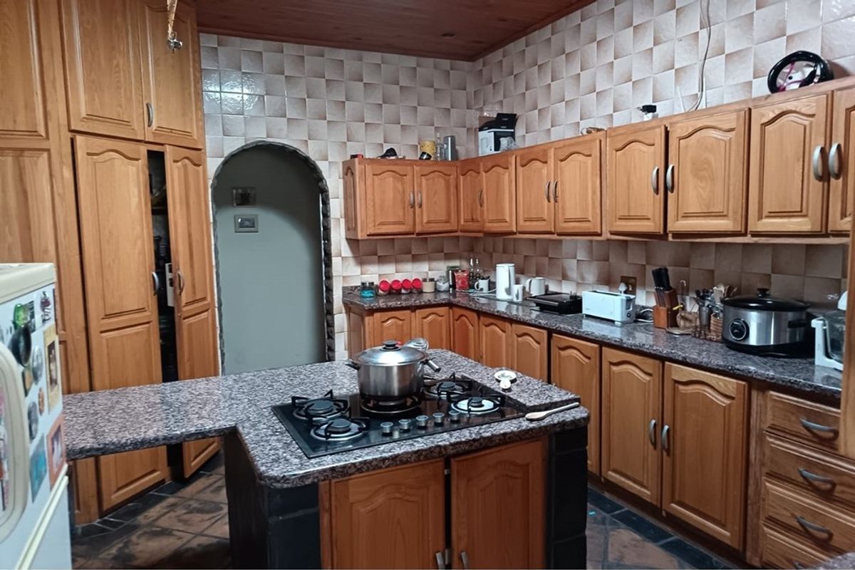 A traditional kitchen featuring extensive wooden cabinetry, granite countertops, a central island with a built-in gas hob, and a distinctive arched doorway.