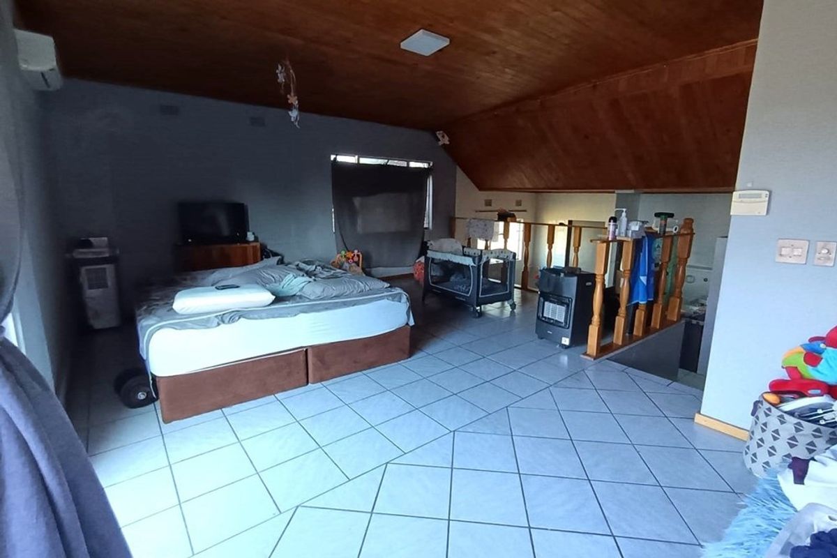 Spacious loft-style bedroom featuring a vaulted timber ceiling, tiled flooring, and an open-plan layout with a wooden balustrade overlooking the lower level.