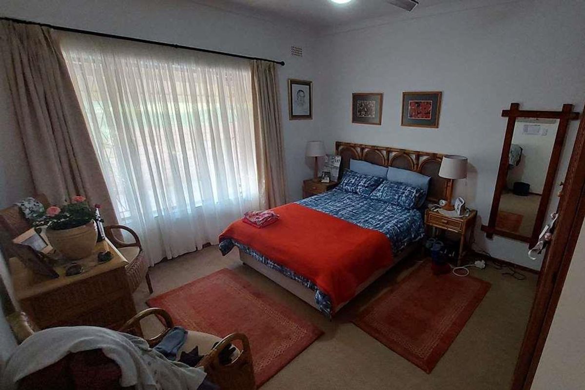 A standard bedroom featuring neutral wall finishes, carpeted flooring, and a large window with curtain rails.