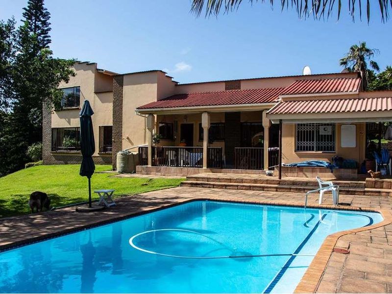 A spacious outdoor pool area featuring a paved deck, a covered patio, and a well-maintained swimming pool set against the rear elevation of the home.