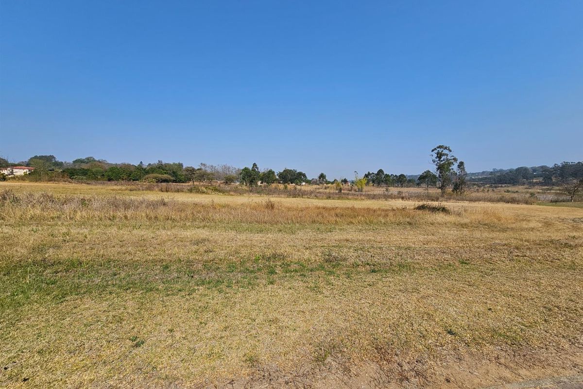 A wide-angle view of a vacant residential plot featuring natural grass terrain and surrounding landscape.