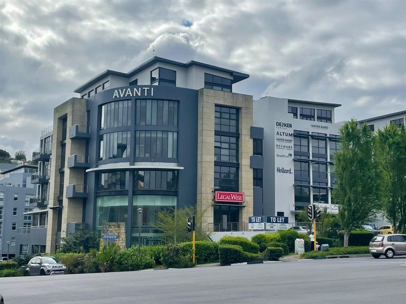 A modern multi-story commercial office building featuring a prominent glass facade, stone accents, and professional signage, situated in a well-maintained business park setting.