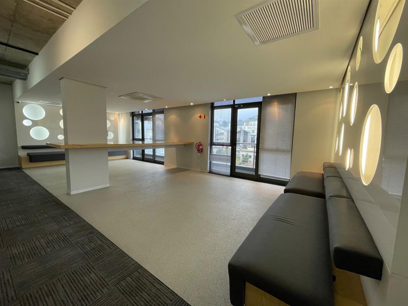 Modern office space featuring integrated wall lighting, built-in bench seating, carpeted and vinyl flooring, and access to a balcony through glass doors.