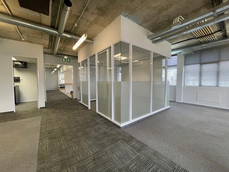 Modern open-plan office space featuring exposed industrial ceilings, glass-partitioned meeting rooms, and durable carpet tile flooring throughout.