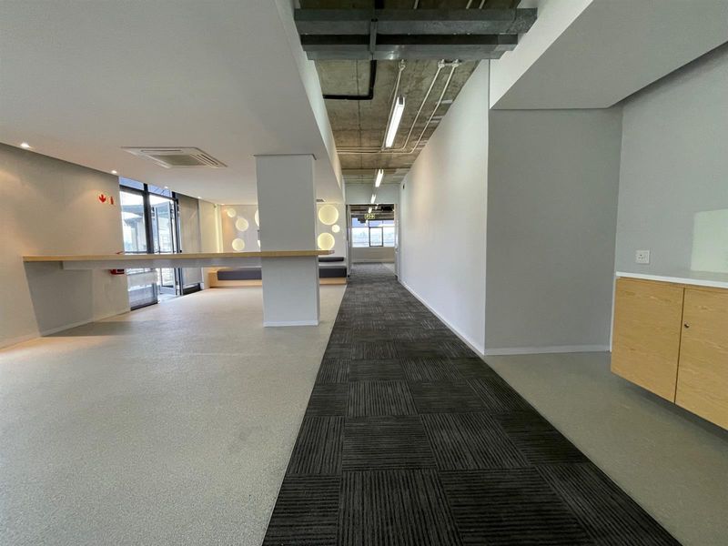 Modern open-plan office space featuring exposed concrete ceilings, linear lighting, a mix of carpet and vinyl flooring, and built-in cabinetry.