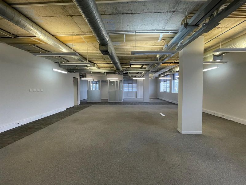 Spacious open-plan office area featuring an industrial aesthetic with exposed concrete ceilings, ducting, and modern linear lighting, providing a versatile workspace.