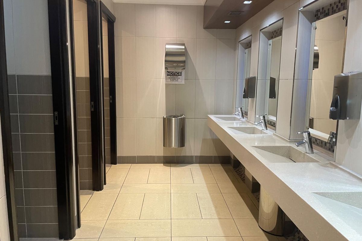 A clean, modern commercial office bathroom featuring multiple vanity sinks, tiled finishes, and private toilet cubicles.
