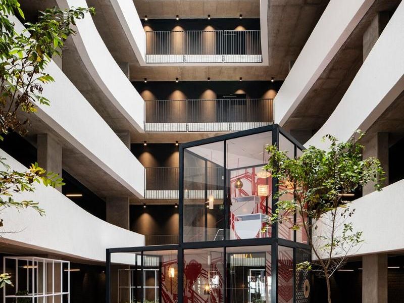 Modern multi-level apartment atrium featuring a central glass-enclosed communal space, timber decking, and integrated planters within a contemporary architectural design.