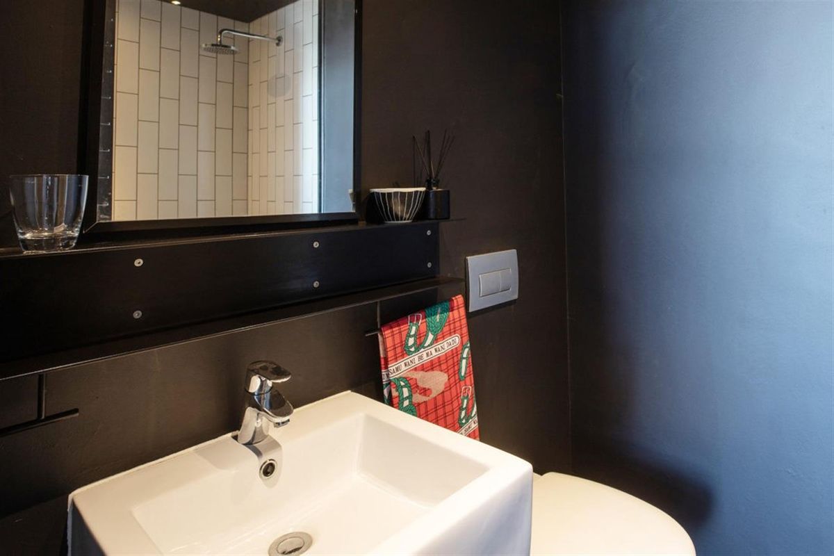 Modern bathroom featuring a wall-mounted basin, chrome fixtures, and a shower enclosure with white subway tiling and dark accent walls.