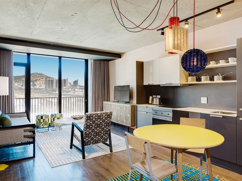 Modern open-plan apartment featuring an exposed concrete ceiling, sleek kitchen cabinetry with integrated appliances, and floor-to-ceiling windows offering expansive city and mountain views.