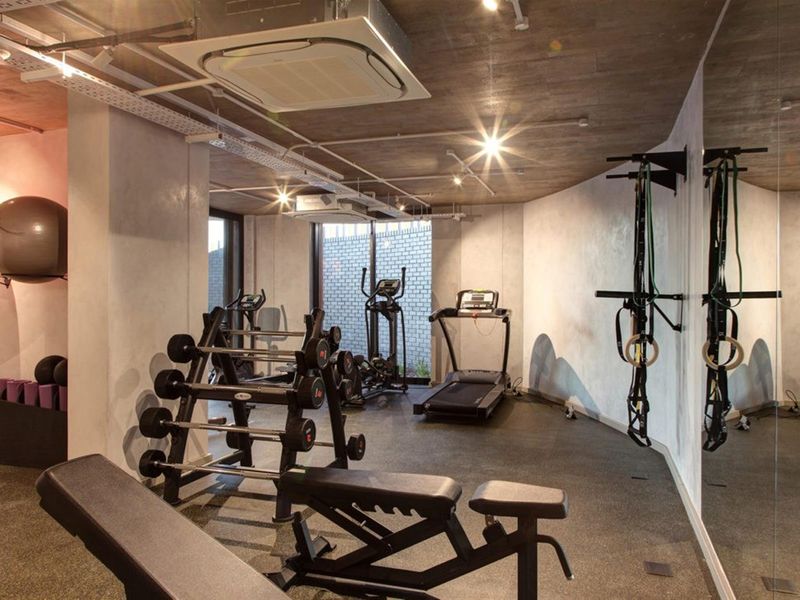 Modern apartment gym facility featuring exposed concrete ceilings, ducted air conditioning, rubberized flooring, and a large mirrored wall for workout sessions.