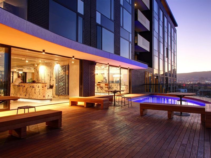 A modern rooftop terrace featuring timber decking, a swimming pool, and seamless indoor-outdoor flow through large glass sliding doors.