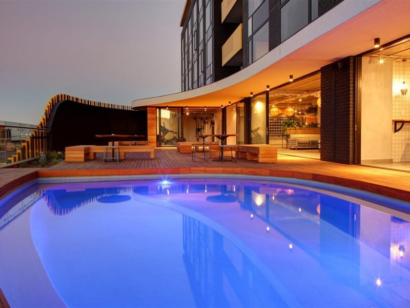 Modern apartment complex pool area featuring a curved swimming pool, timber decking, and seamless indoor-outdoor flow through large sliding glass doors.