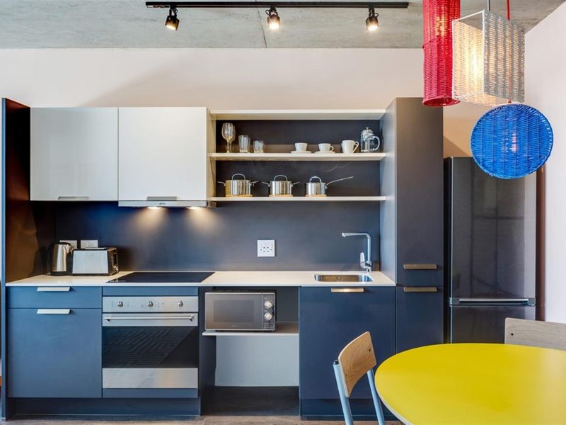 Modern kitchen featuring dark blue cabinetry, white countertops, built-in oven and cooktop, and an industrial-style exposed concrete ceiling with track lighting.