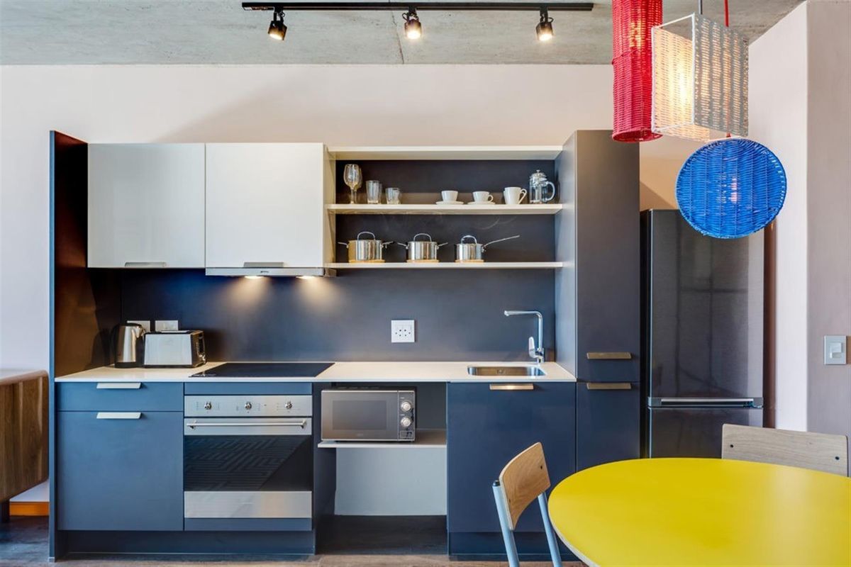 Modern kitchen featuring dark blue cabinetry, white countertops, built-in oven and cooktop, and an industrial-style exposed concrete ceiling with track lighting.