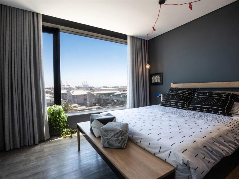 Modern bedroom featuring floor-to-ceiling windows with expansive urban views, sleek laminate flooring, and contemporary dark accent wall.