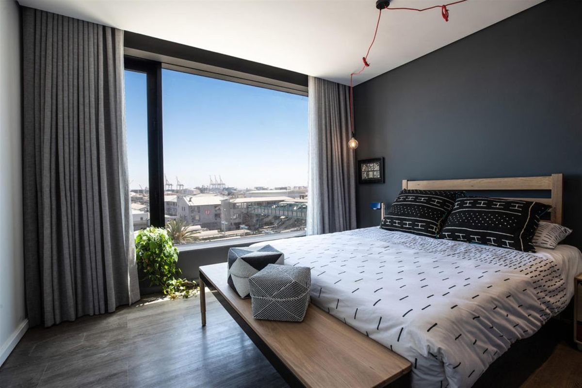 Modern bedroom featuring floor-to-ceiling windows with expansive urban views, sleek laminate flooring, and contemporary dark accent wall.