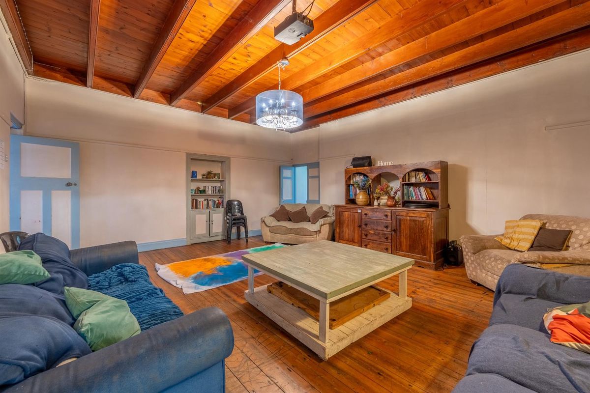 Spacious living room featuring exposed timber beam ceilings, polished wooden flooring, and a built-in wall shelving unit.