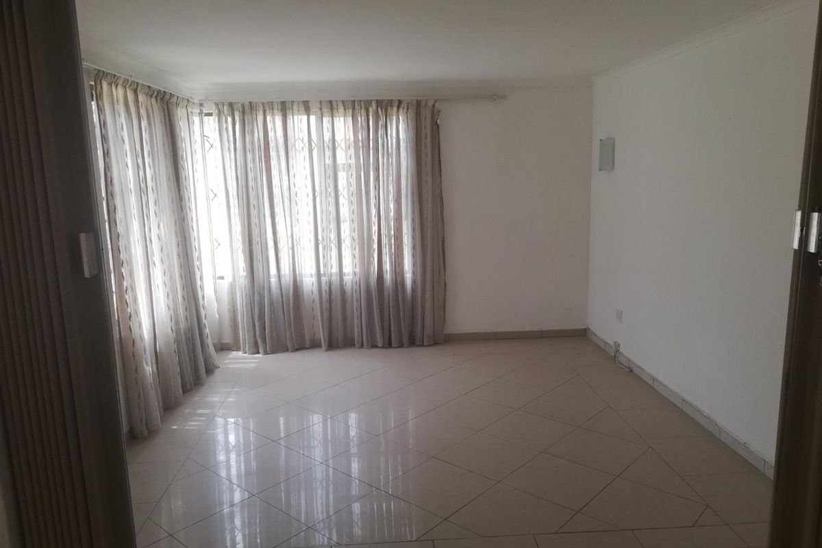 A bright, empty living room featuring neutral tiled flooring and large windows with curtains, offering a clean and versatile space.