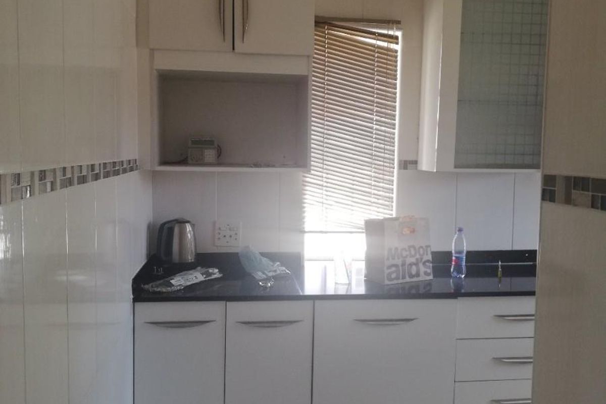 A functional kitchen featuring white cabinetry, dark stone countertops, tiled walls with decorative accents, and tiled flooring.