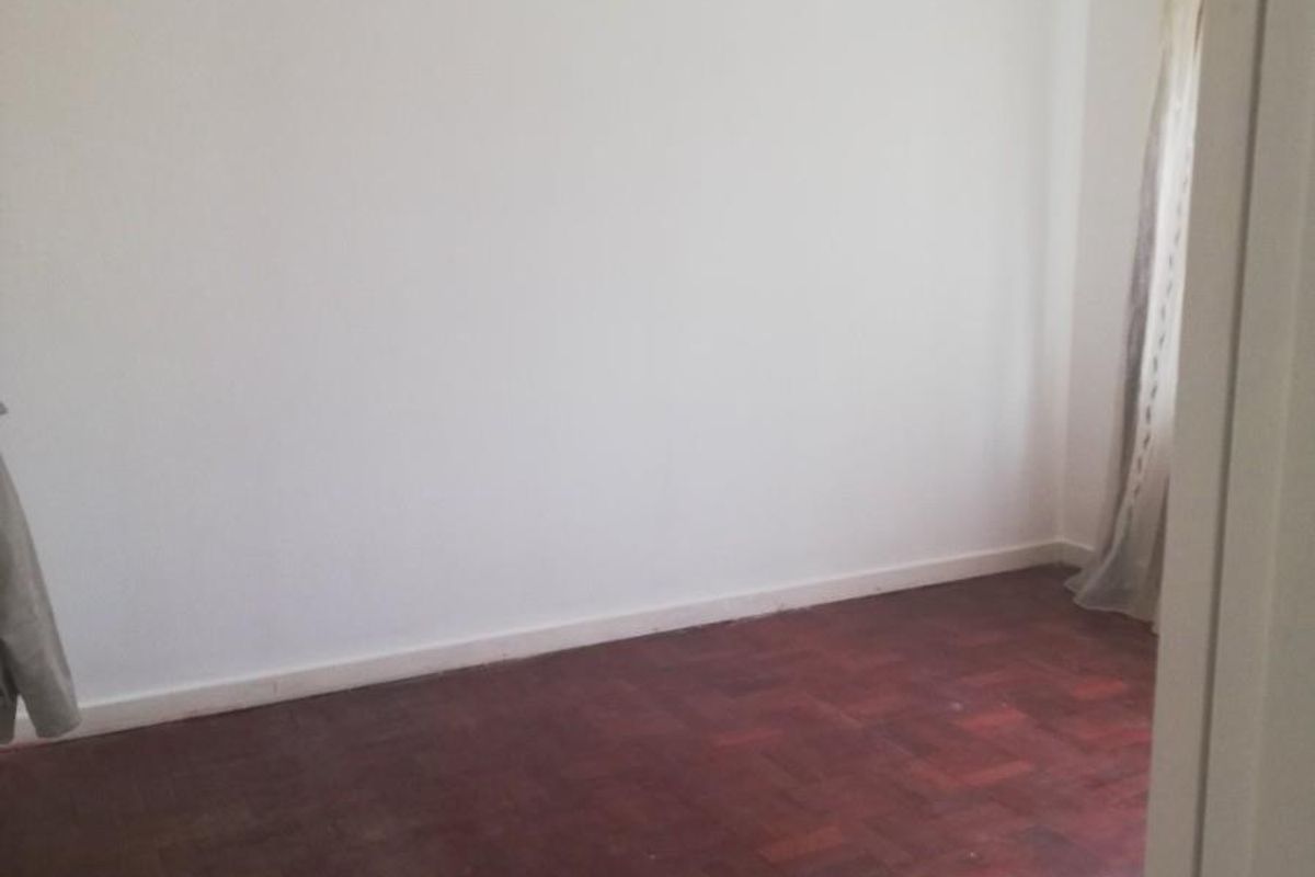An empty bedroom featuring original parquet timber flooring, neutral white walls, and recessed ceiling lighting.