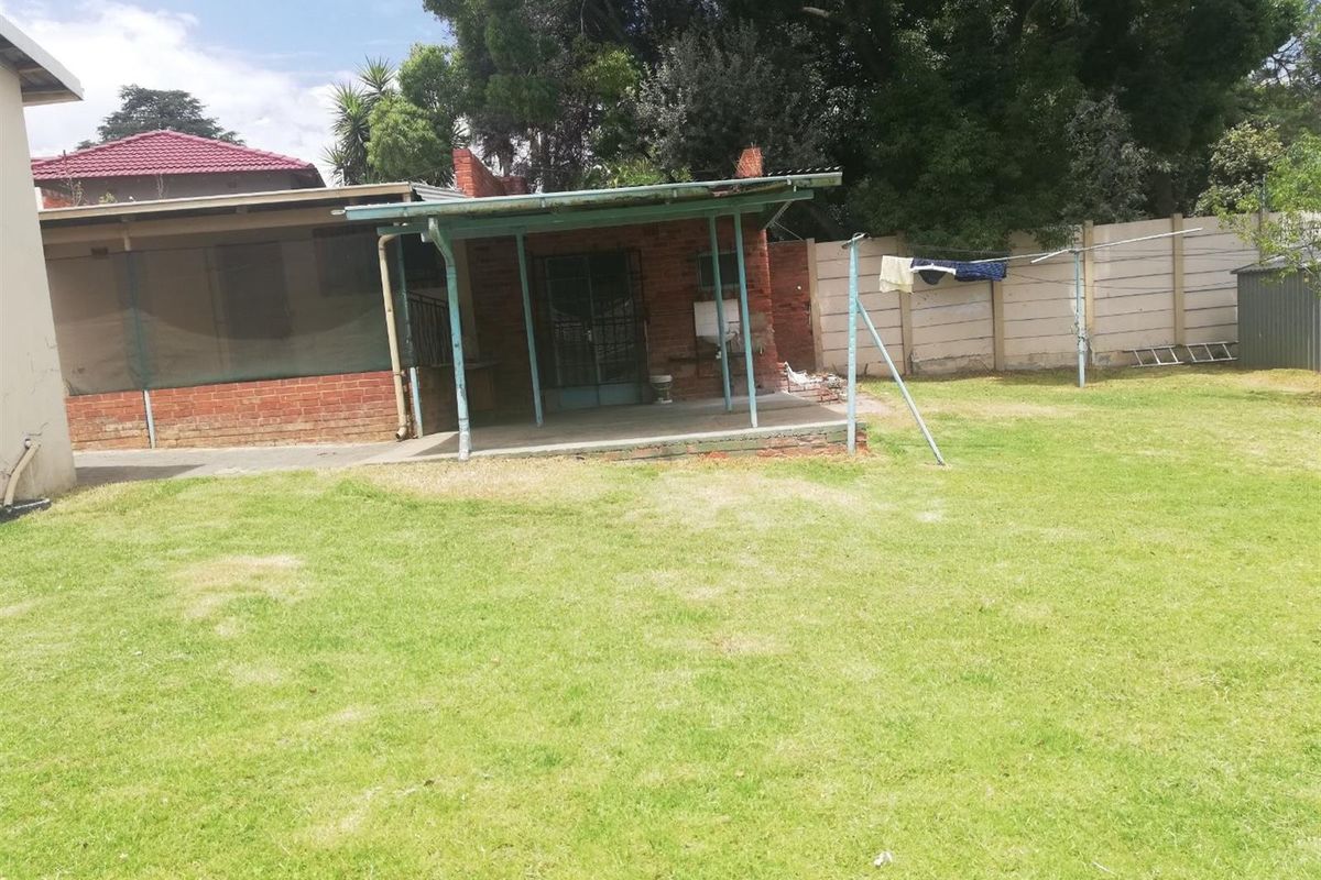 Rear view of the property featuring a covered patio area, brick exterior walls, and a spacious backyard with perimeter wall fencing.