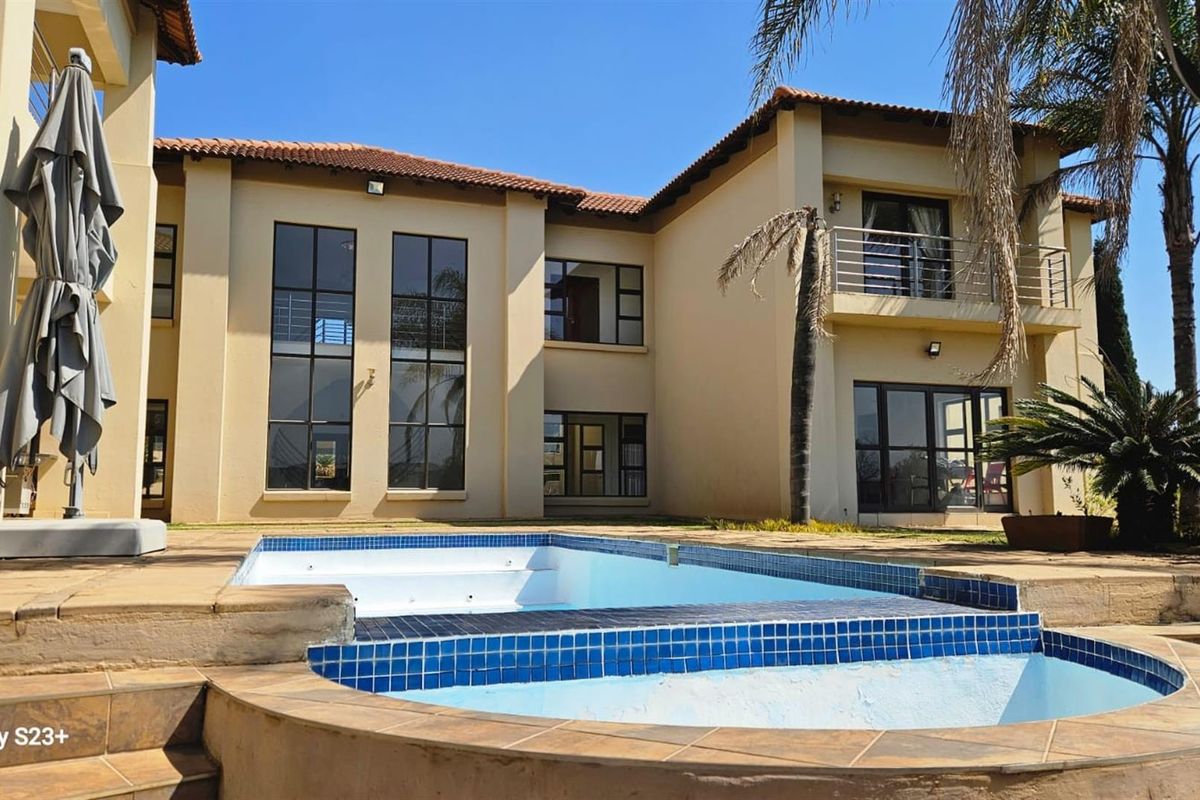 Rear view of a two-story residential property featuring a swimming pool, tiled patio area, and a balcony overlooking the garden.