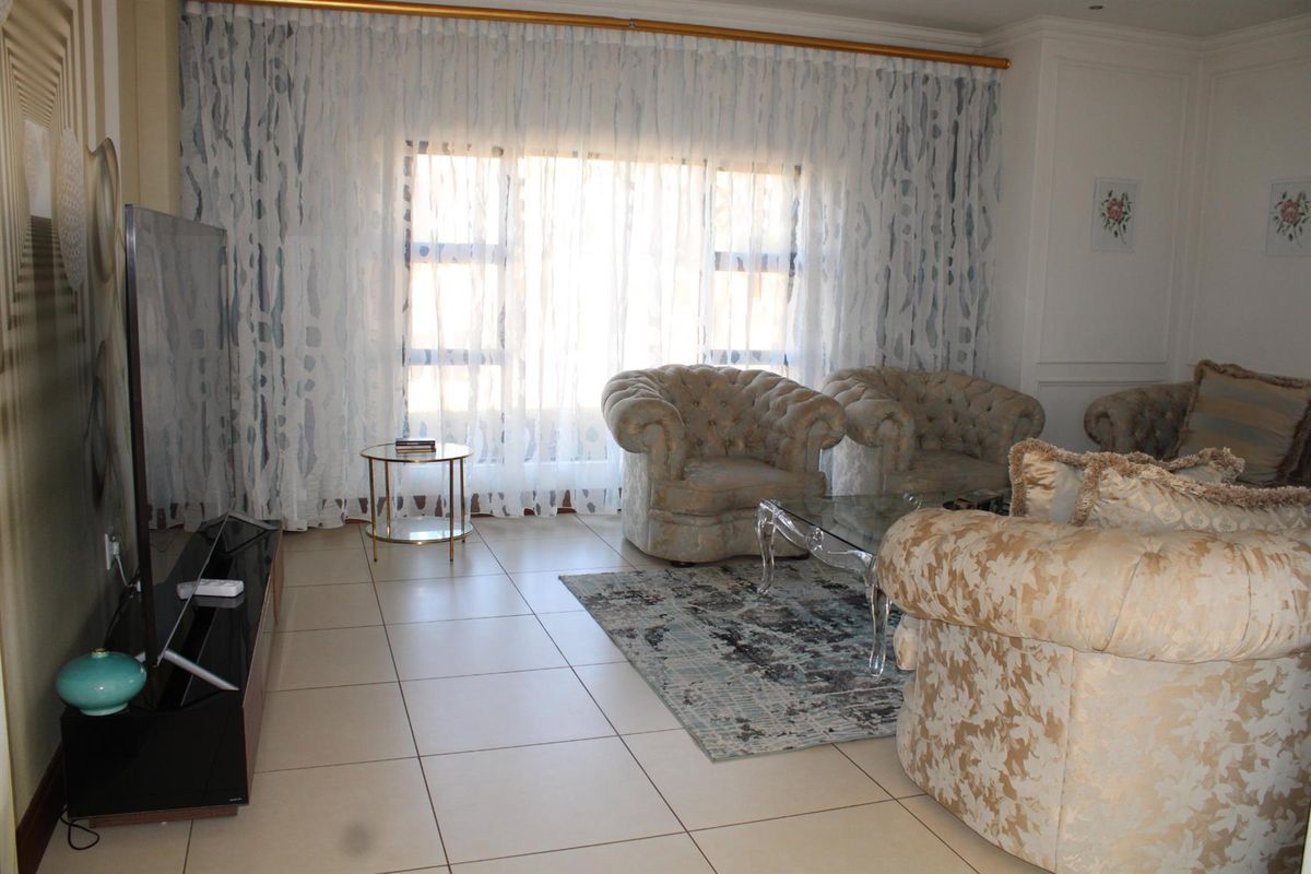 A comfortable living room featuring large windows with floor-to-ceiling curtains and neutral tiled flooring.