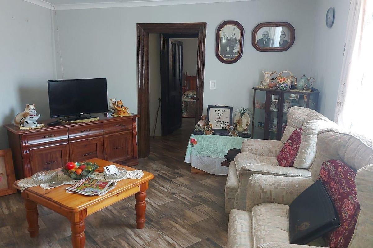 A living room featuring wood-look tile flooring and traditional timber door frames, providing access to an adjacent bedroom.