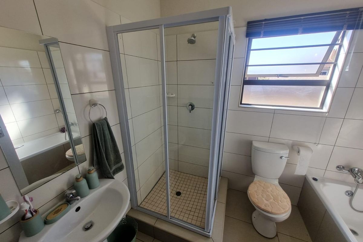 A functional bathroom featuring a glass-enclosed shower, a separate bathtub, a pedestal basin, and a toilet with tiled walls and flooring.