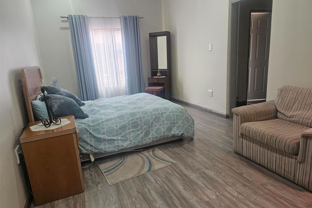 A spacious bedroom featuring modern wood-look laminate flooring, neutral wall tones, and a window with curtain treatments.