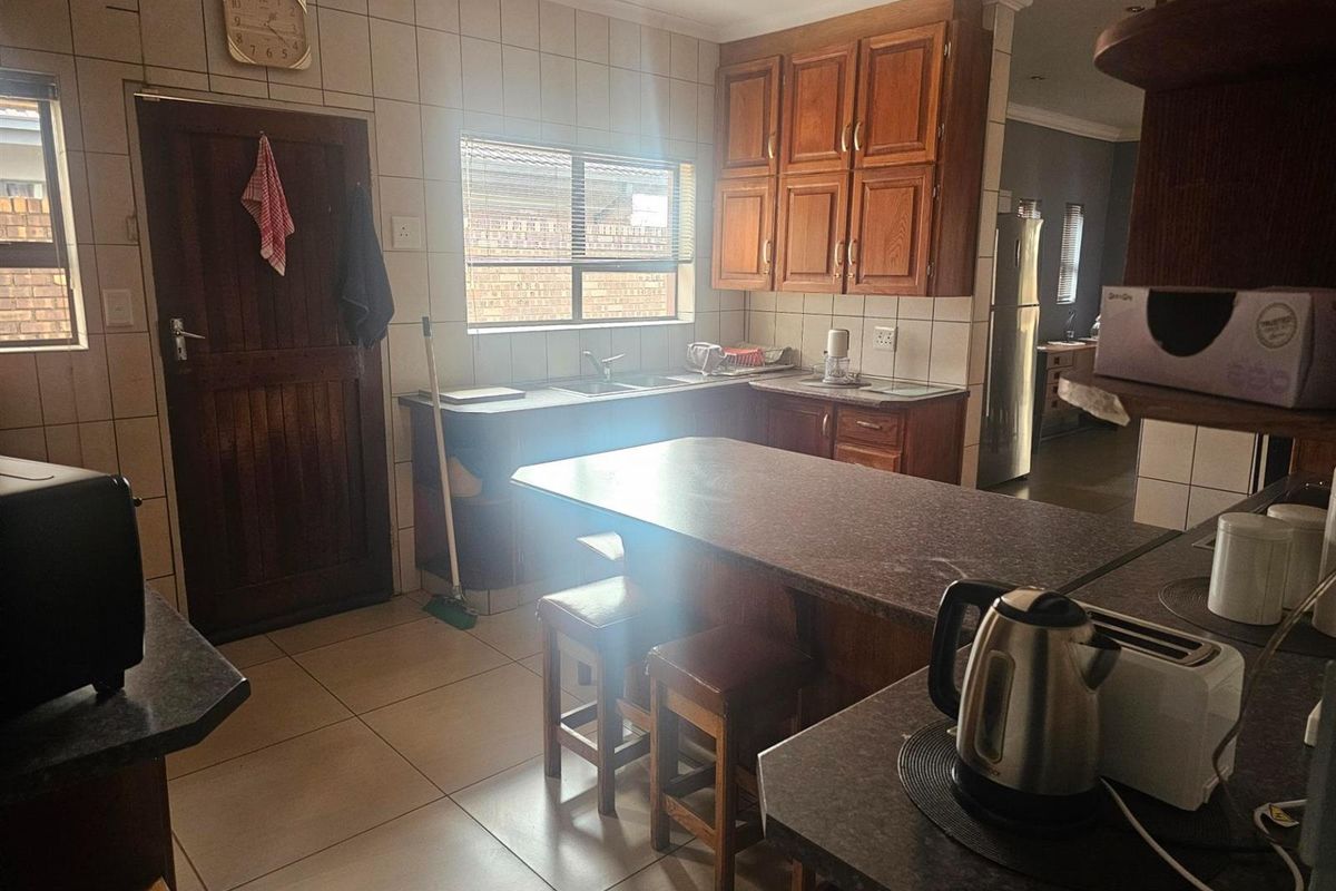 A functional kitchen featuring wooden cabinetry, tiled walls, a central breakfast island, and tiled flooring with direct access to an exterior door.