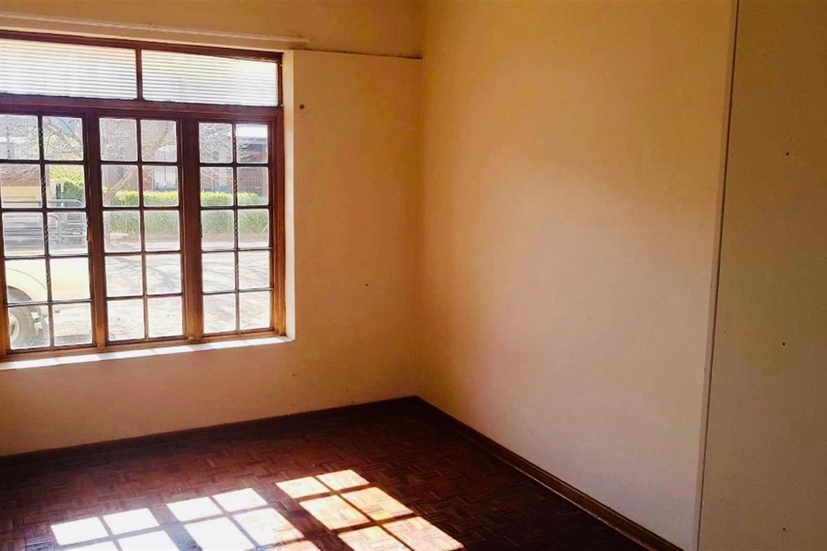 An empty bedroom featuring original parquet flooring, a timber-framed window, and a built-in cupboard, offering a blank canvas for renovation.