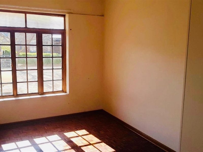 An empty bedroom featuring original parquet flooring, a timber-framed window, and a built-in cupboard, offering a blank canvas for renovation.