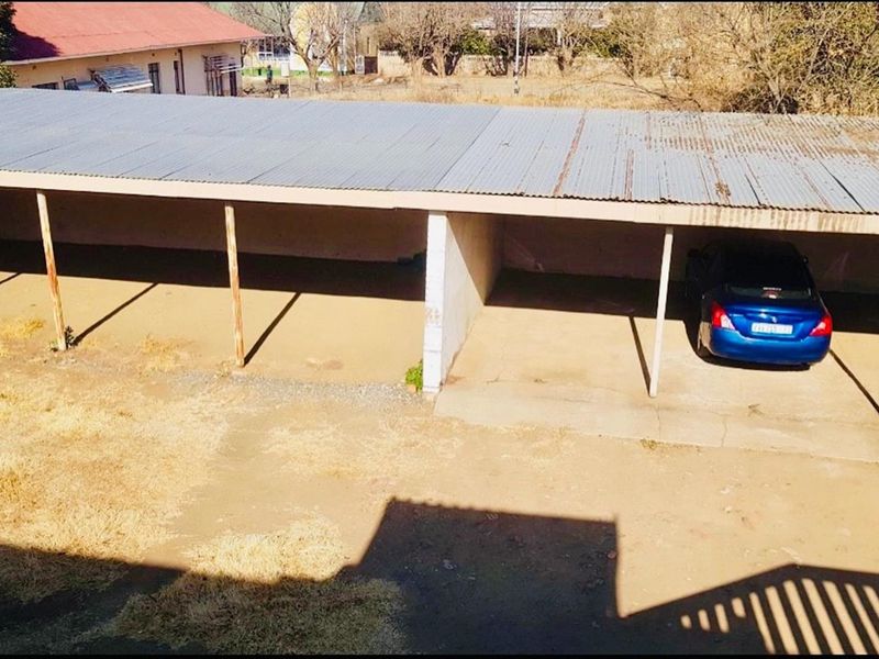 Open-sided carport structure with corrugated metal roofing and concrete flooring, providing covered parking space.