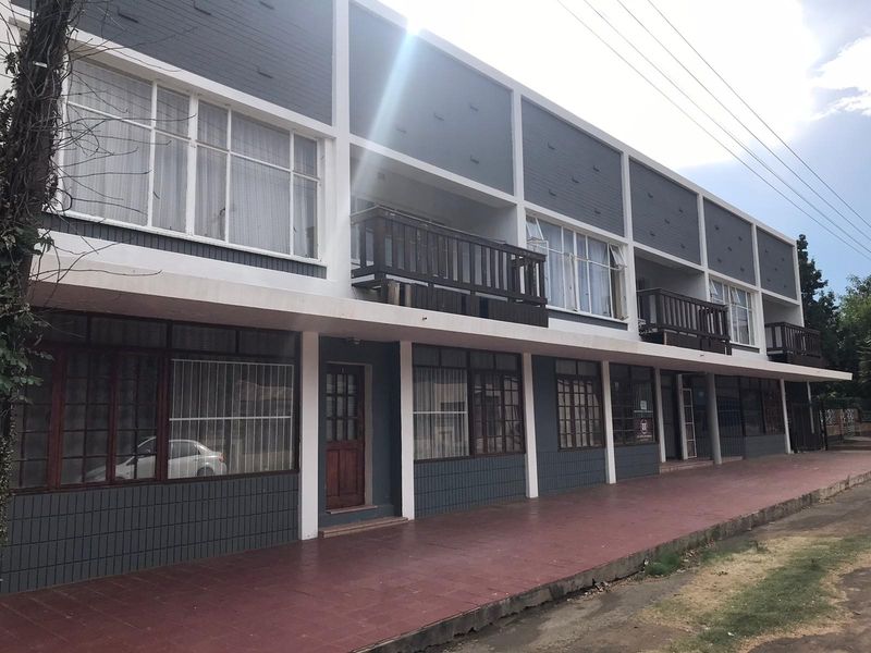 Front elevation of a multi-story residential building featuring a tiled walkway, ground floor access points, and upper-level balconies with timber railings.