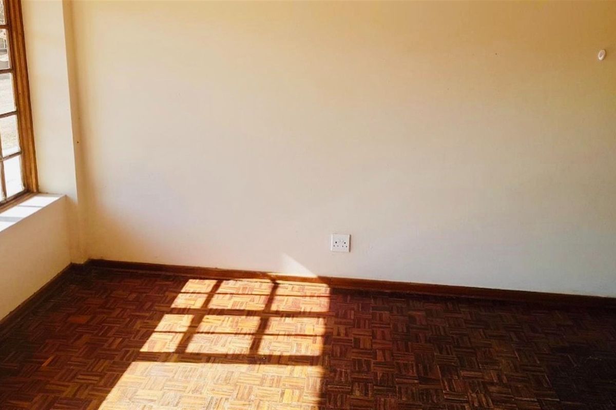 An empty living room featuring classic parquet flooring and a large timber-framed window that allows for natural light.