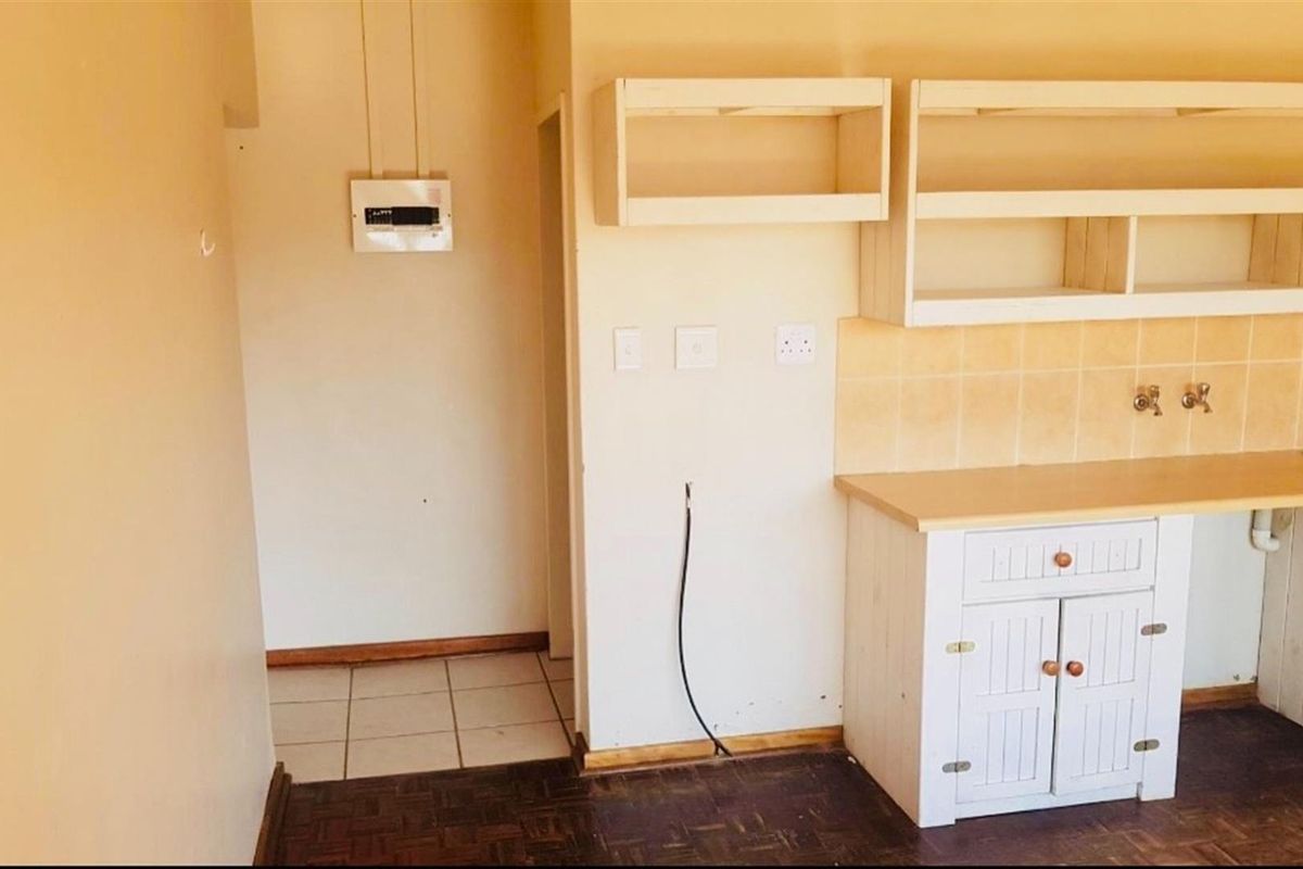 A basic kitchen area featuring built-in cabinetry, a tiled backsplash, and a sink, with a mix of parquet and tiled flooring.