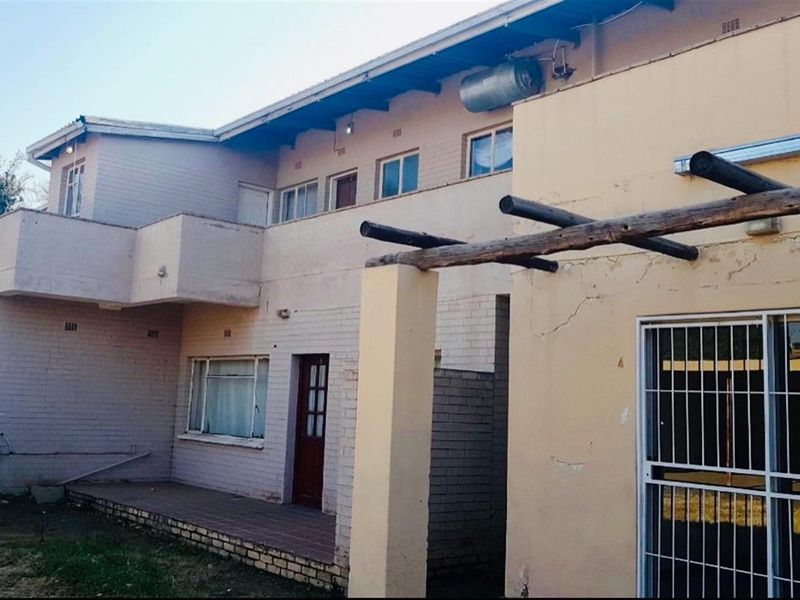Rear elevation of a multi-story house featuring a timber pergola, balcony, and external staircase, showing signs of wear and required maintenance.