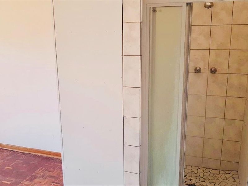 A functional bathroom featuring a shower enclosure with tiled walls and mosaic flooring, adjacent to a room with parquet flooring.